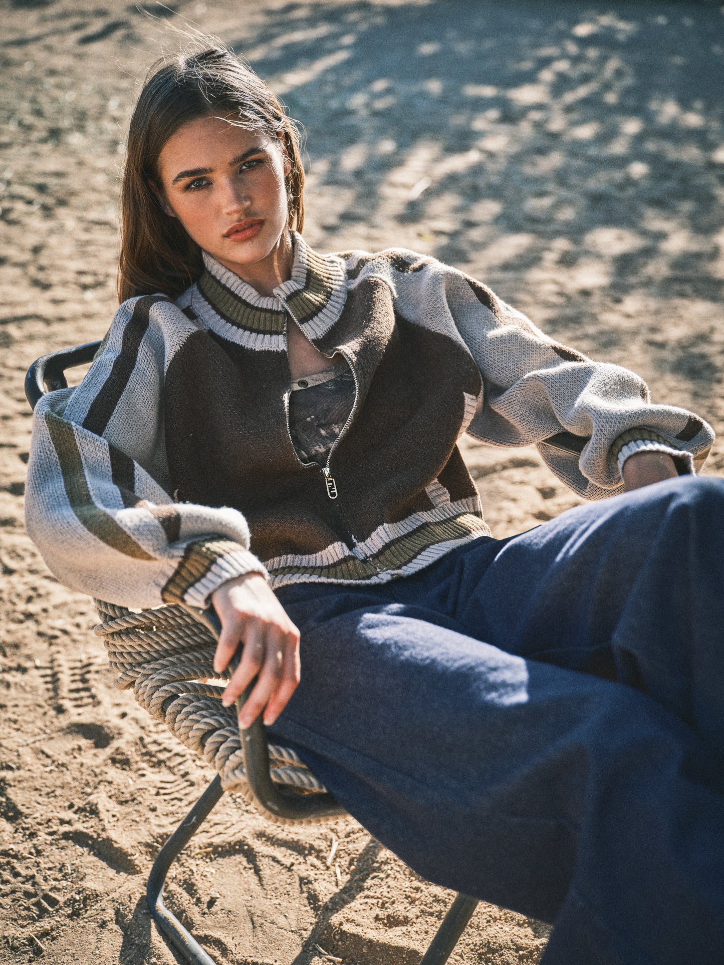 Brown and cream zip-up sweater with striped detailing, worn by a model outdoors, showcasing relaxed style.