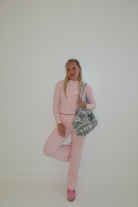 Person wearing a pink outfit with a patterned bag on a plain background