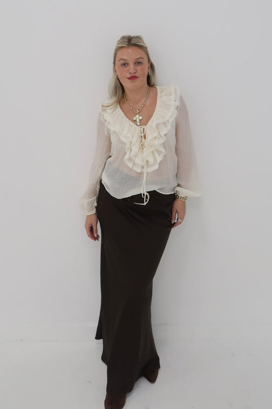 Model wearing an ivory ruffle blouse and brown maxi skirt, showcasing a chic, layered look.