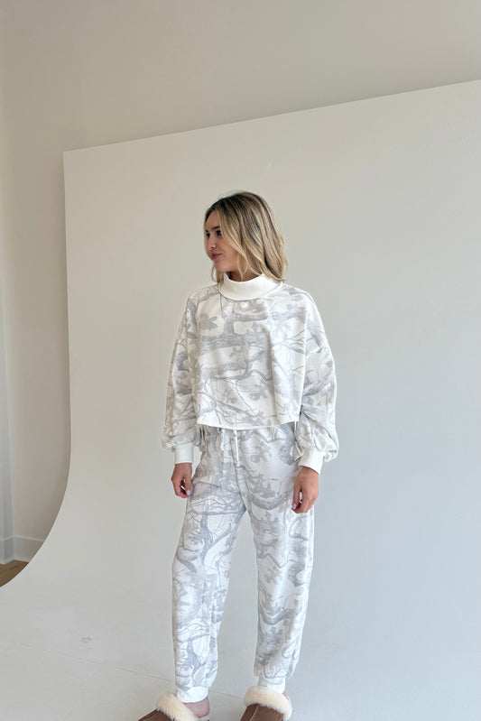 Woman wearing a white and gray patterned outfit against a plain background