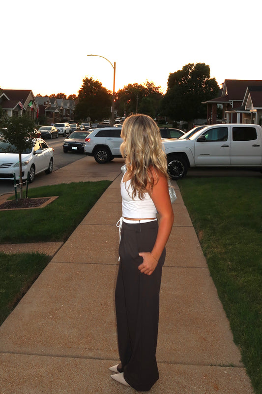 Fashionable woman in a white top and dark wide-leg pants, standing on a sidewalk at sunset.