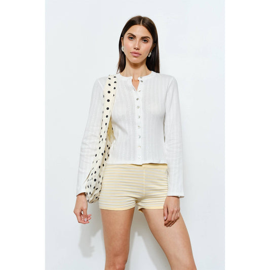 White long-sleeve ribbed button-up top paired with striped yellow shorts.
