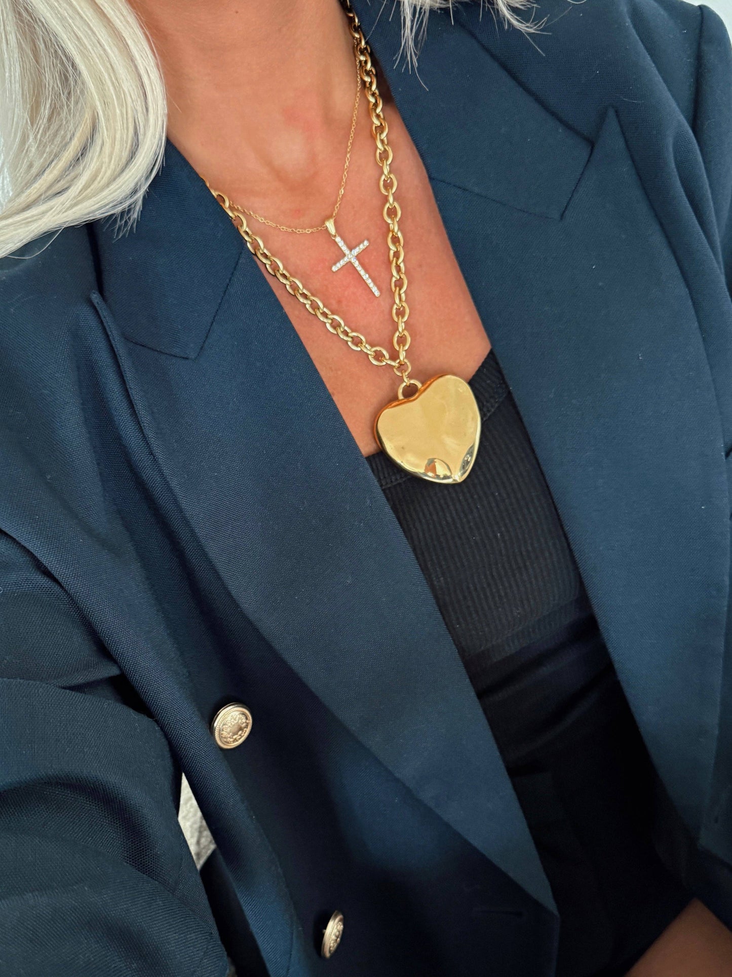Person wearing a navy blazer with gold jewelry including a necklace and pendant.