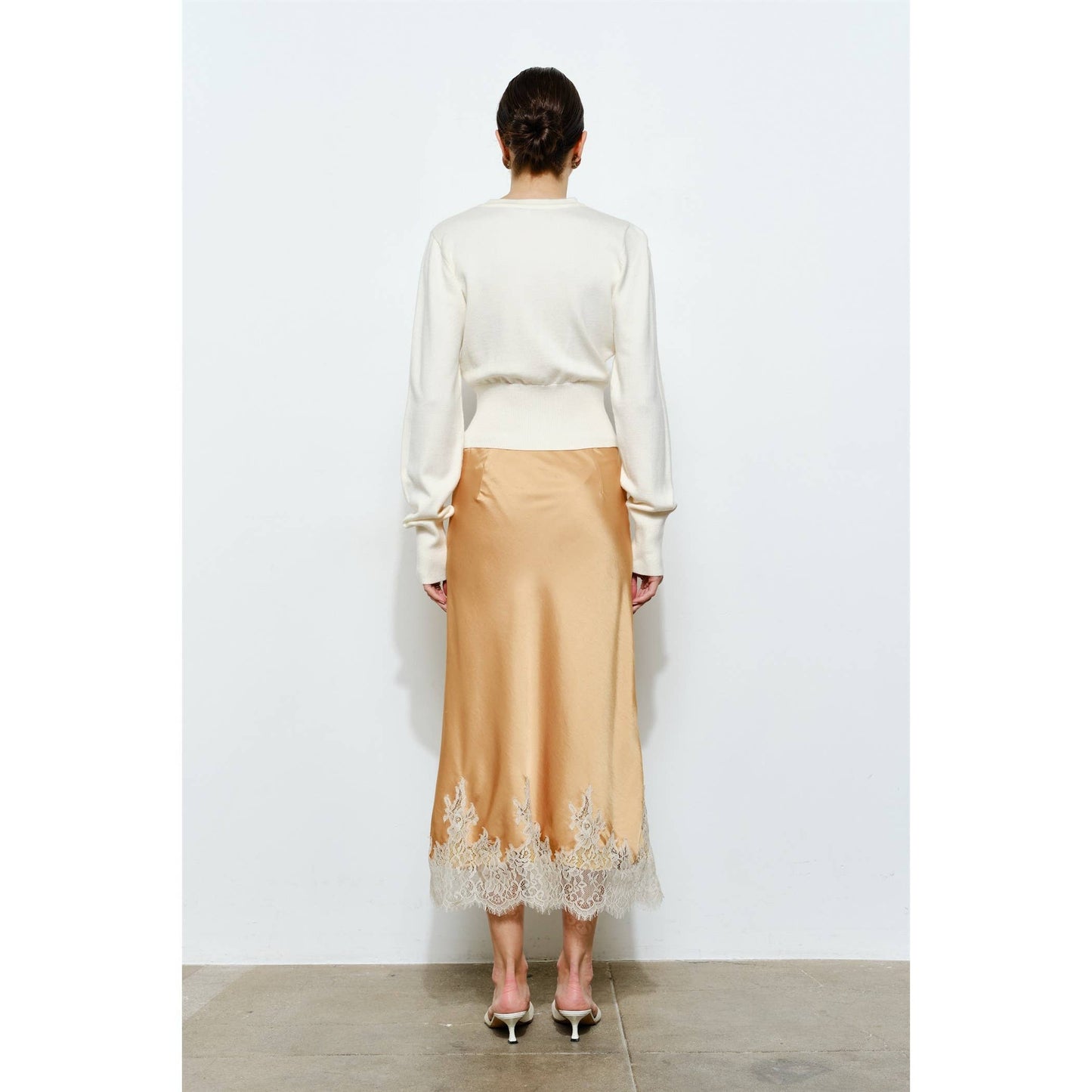 Woman's back view in cream sweater and peach satin skirt with lace trim, ideal for elegant occasions.