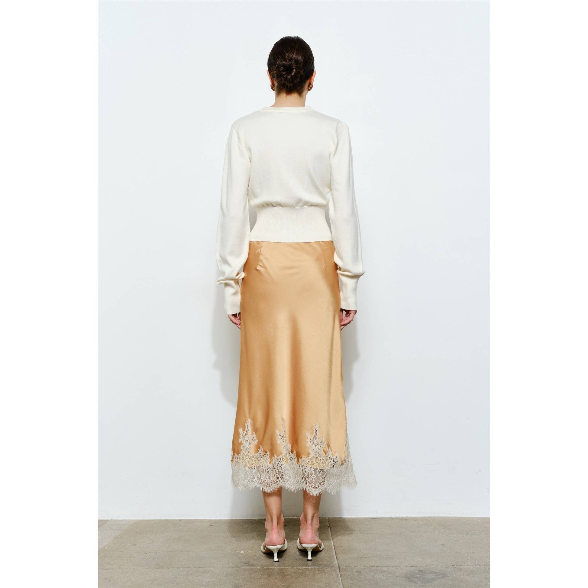 Woman's back view in cream sweater and peach satin skirt with lace trim, ideal for elegant occasions.