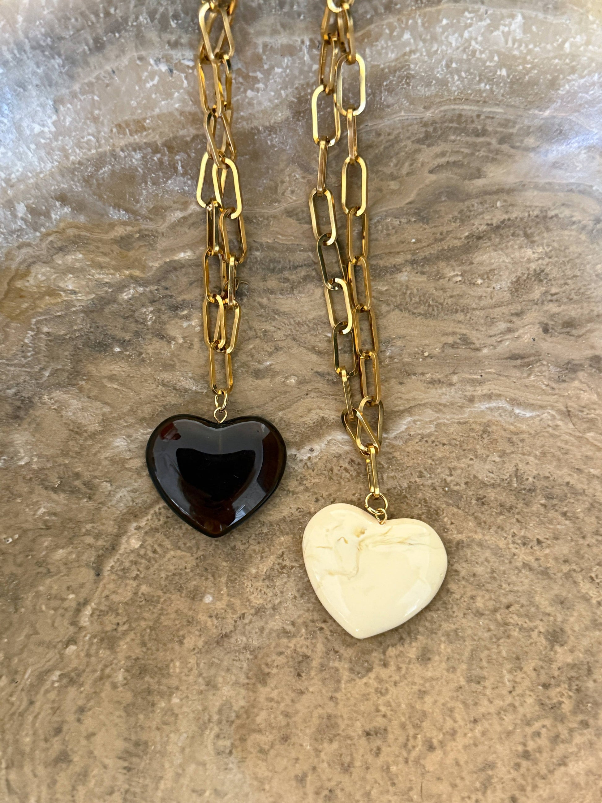 Two heart-shaped pendants on a gold chain against a stone background