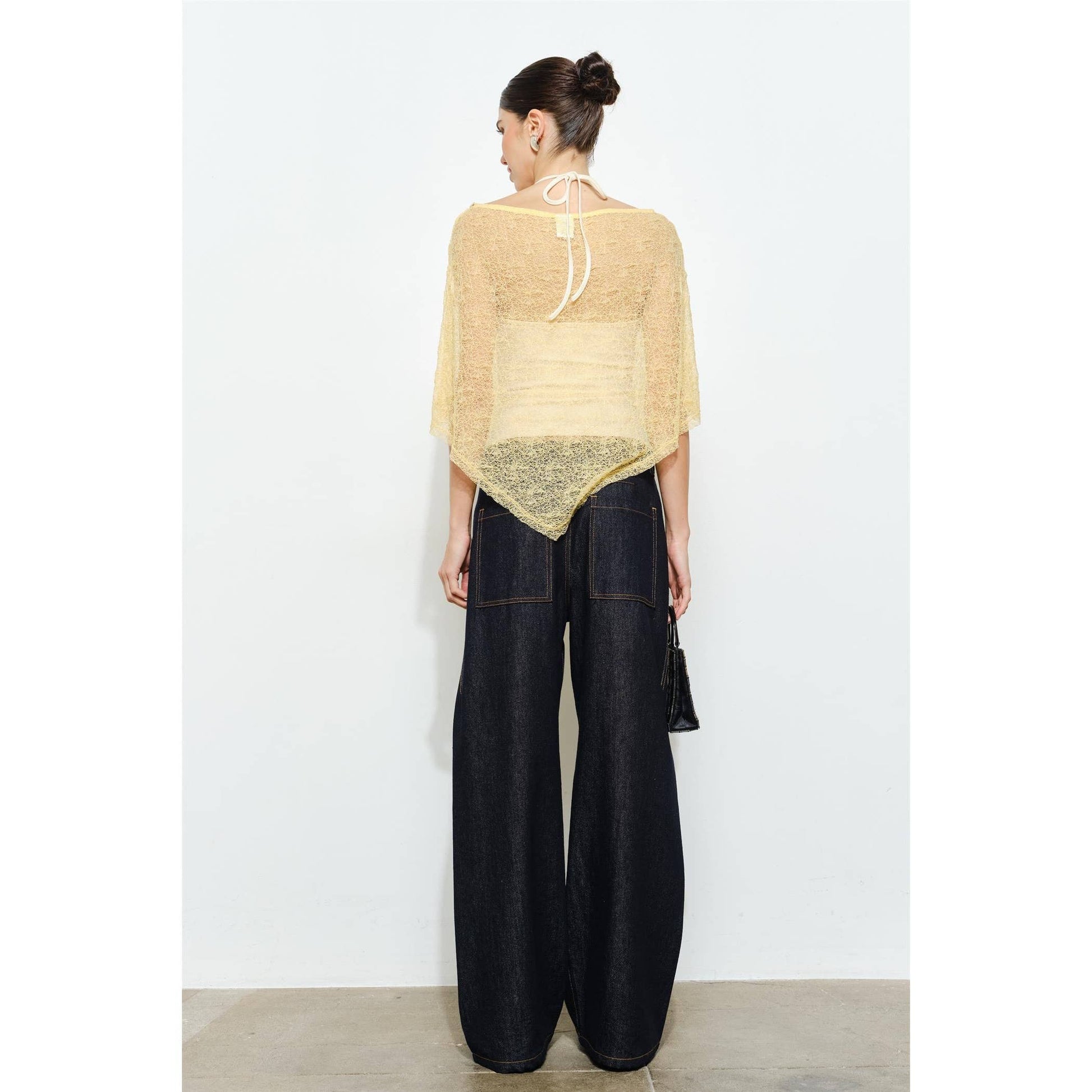 Woman wearing a beige poncho and black wide-leg pants against a white background
