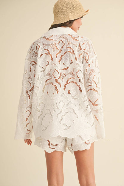 Person wearing a white lace cover-up with orange patterns on a beige background