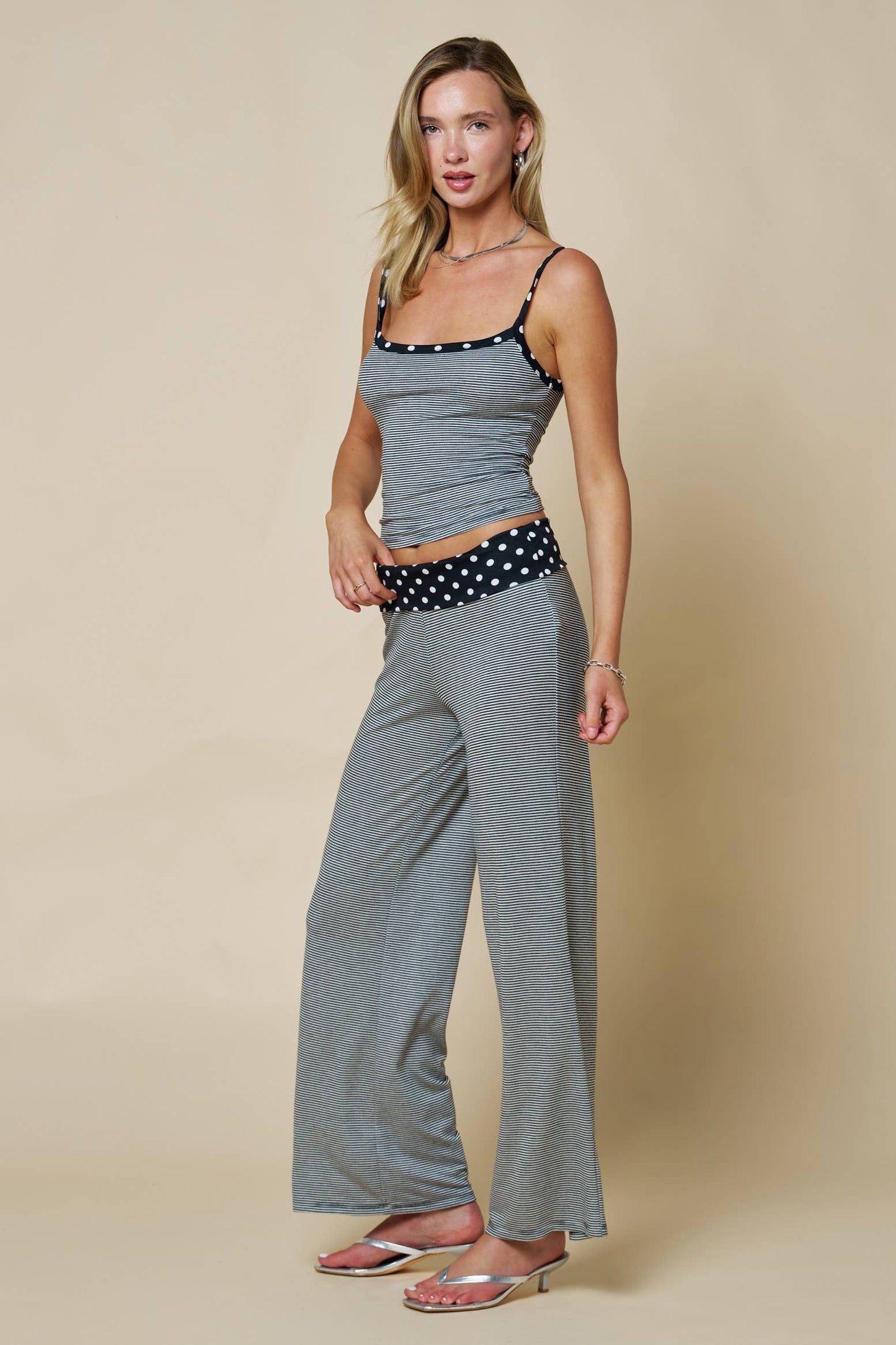 Woman wearing a black tank top and wide-leg pants with a polka dot waistband on a beige background