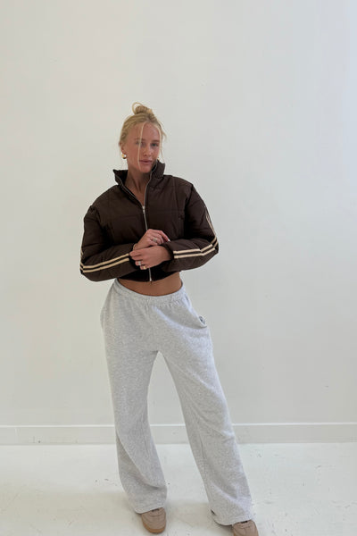 Brown cropped puffer jacket with zip and stripes, paired with gray sweatpants, perfect for casual wear.