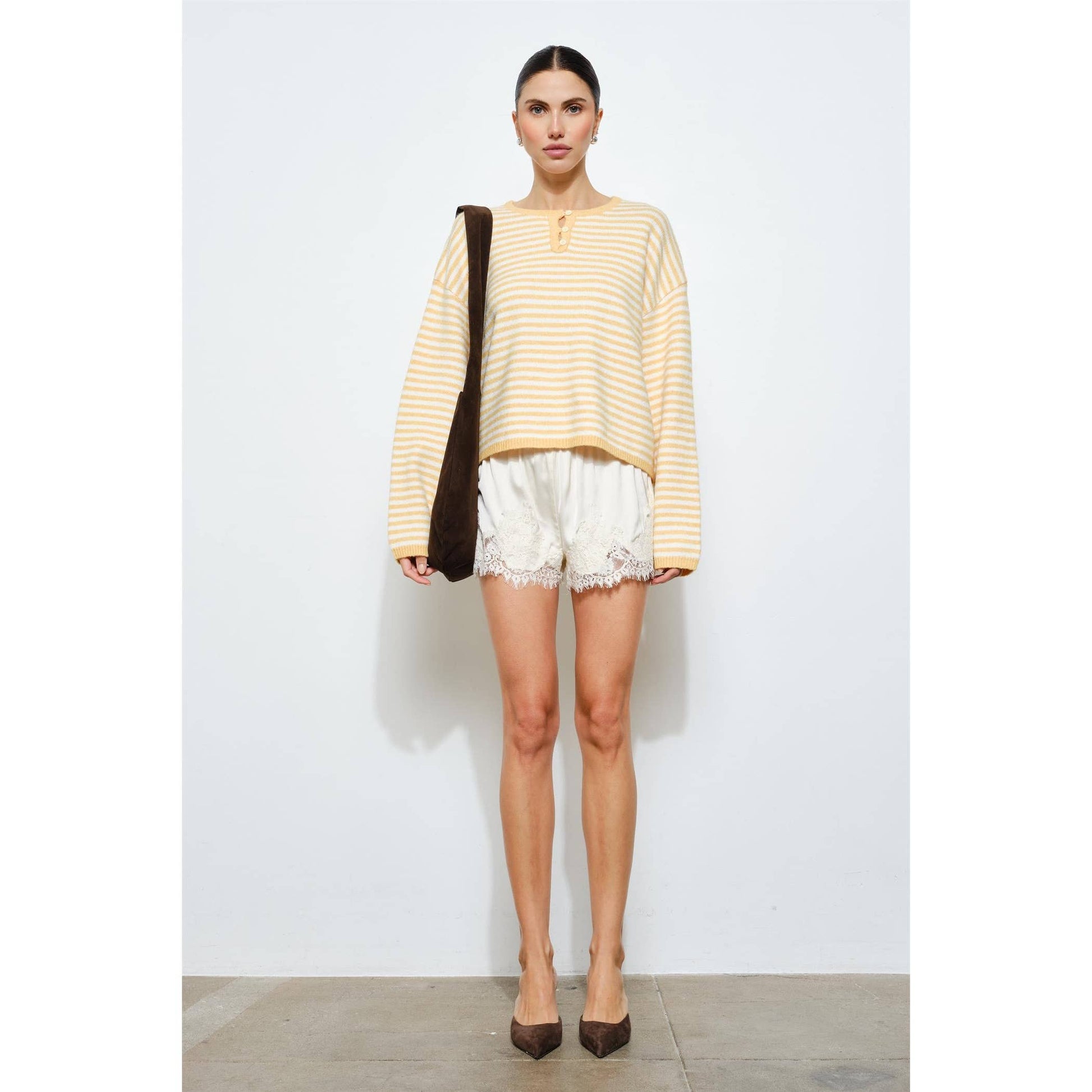 Woman wearing a striped yellow and white top with lace-trimmed shorts on a plain background