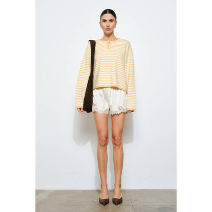 Woman wearing a striped yellow and white top with lace-trimmed shorts on a plain background