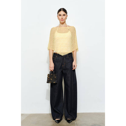 Woman wearing a yellow top and black pants holding a black handbag on a white background
