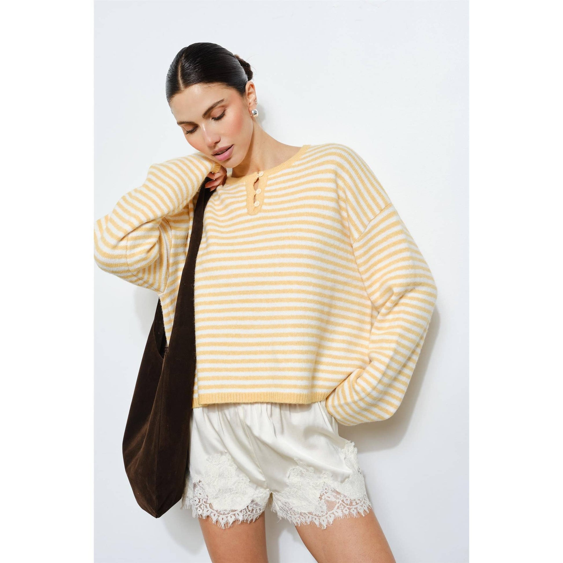 Woman wearing a yellow and white striped sweater and white shorts against a light gray background