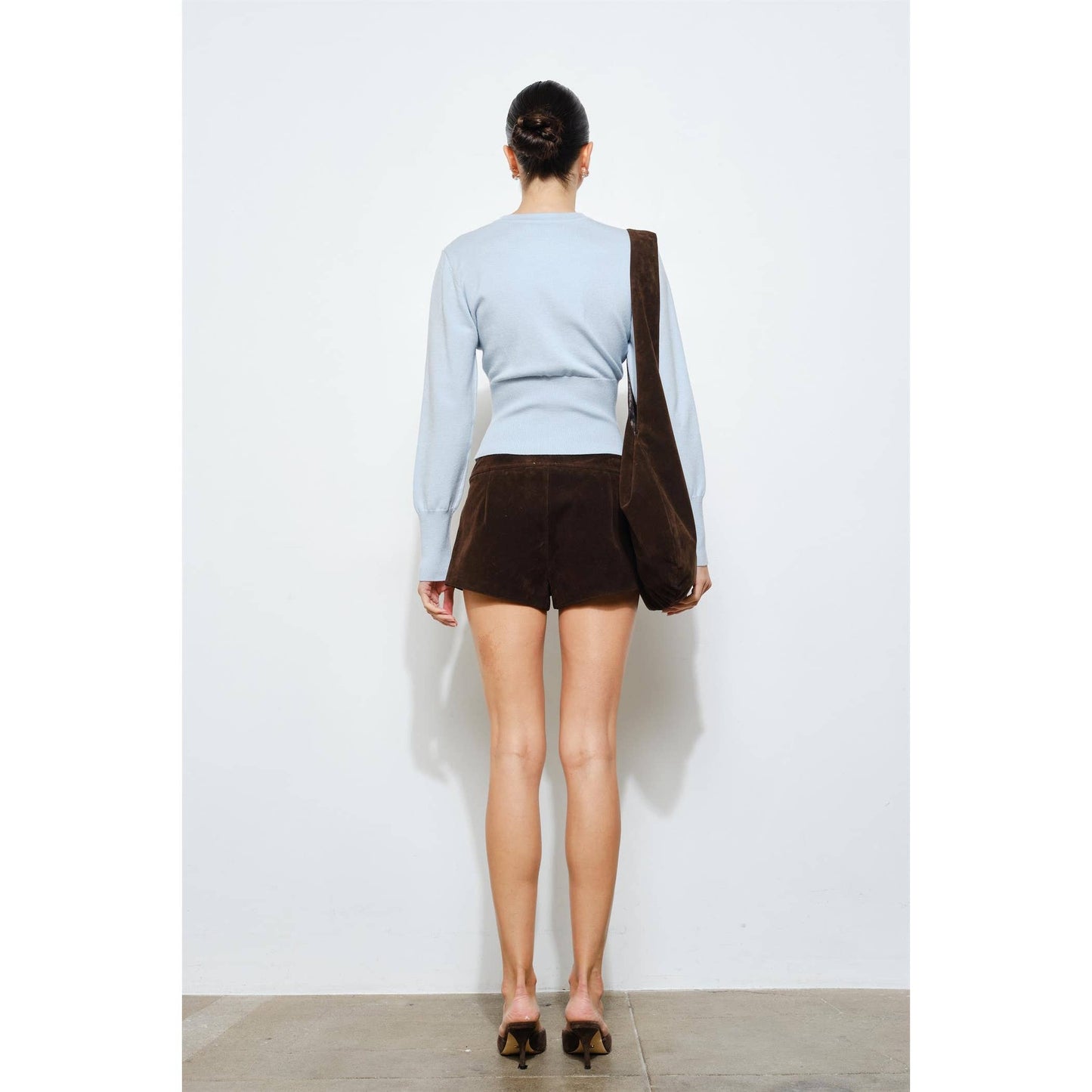 Model wearing a light blue sweater and brown suede shorts, showcasing a chic casual style from the back.