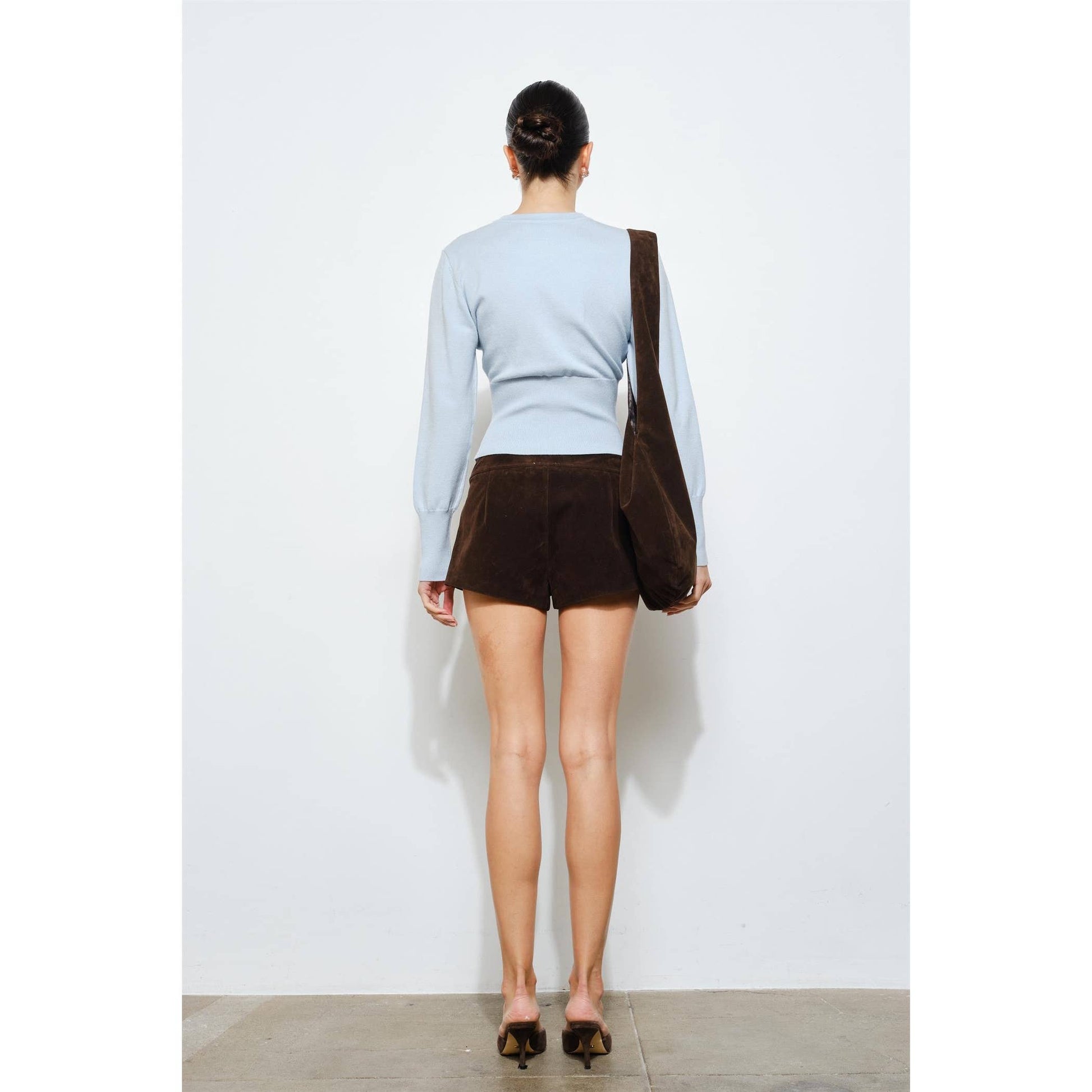 Model wearing a light blue sweater and brown suede shorts, showcasing a chic casual style from the back.