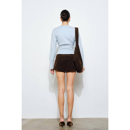 Model wearing a light blue sweater and brown suede shorts, showcasing a chic casual style from the back.