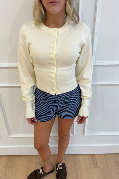 Women's light yellow button-up cardigan sweater with long sleeves, paired with blue striped shorts.