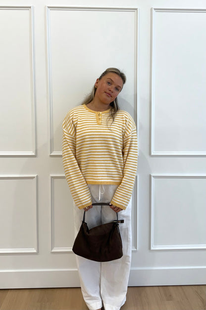Yellow striped sweater with button detail, paired with white pants and a brown handbag.