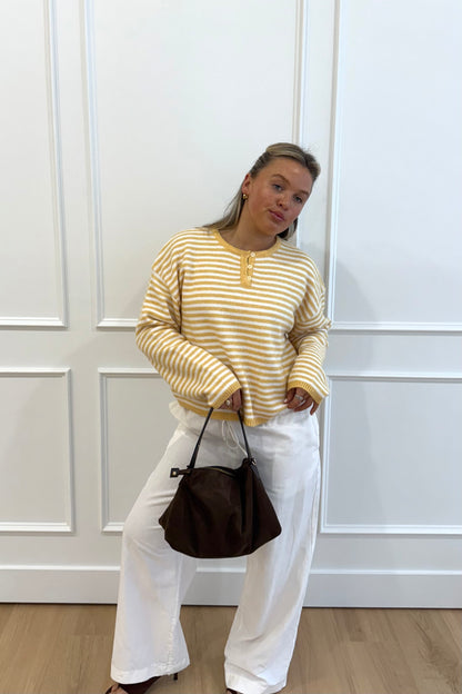 Woman in yellow and white striped sweater, paired with white wide-leg pants and a brown handbag.