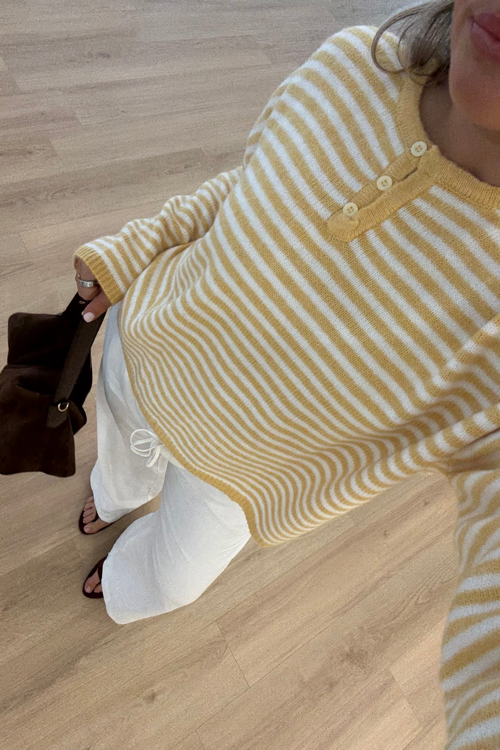 Yellow and white striped sweater, soft knit fabric, featuring round neckline and button detail, paired with white pants.