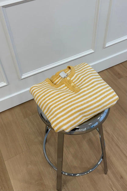 Yellow and white striped sweater folded on a chrome stool, featuring a henley style neckline.