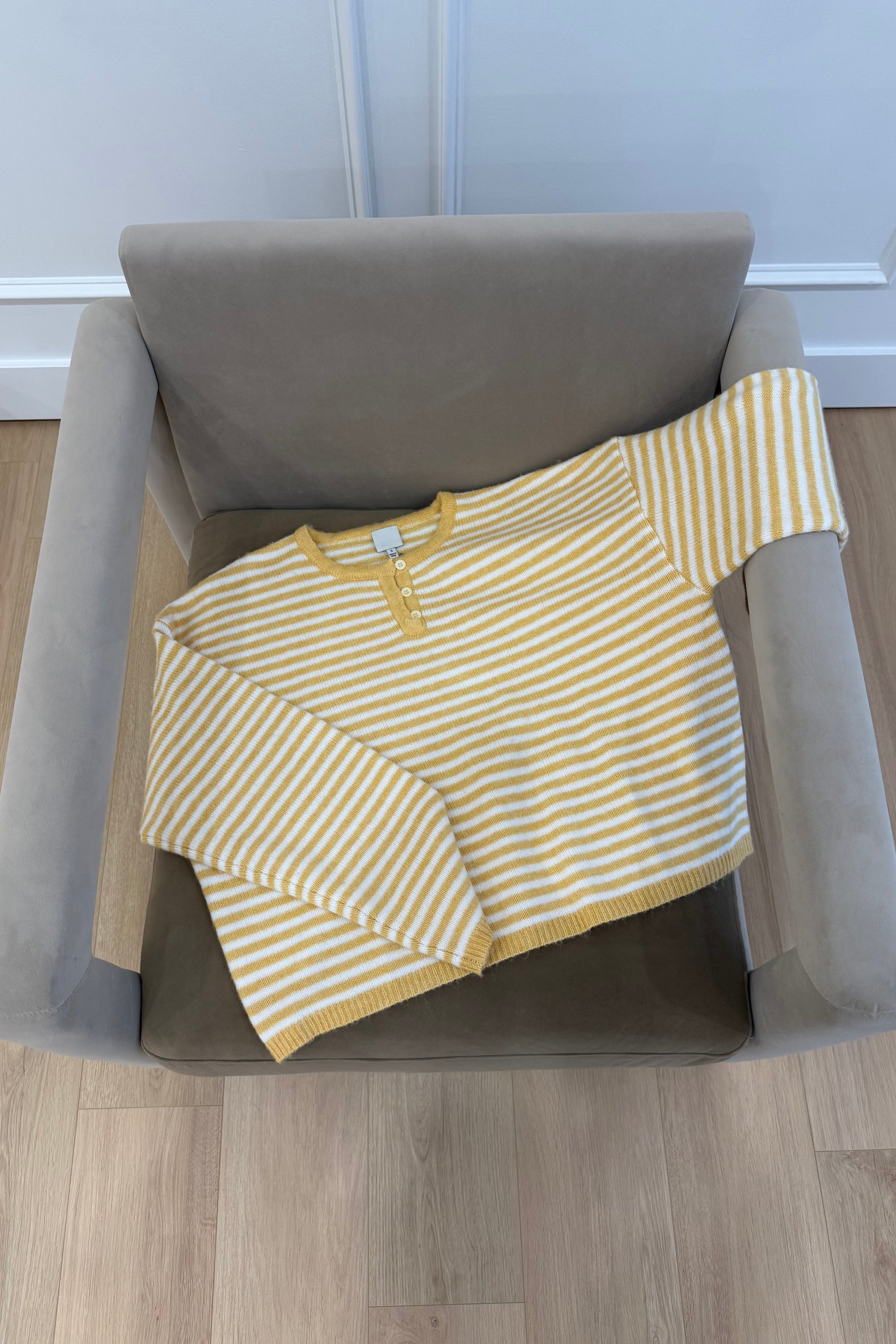 Yellow and white striped knit sweater with a round neck and button detail, perfect for casual wear.