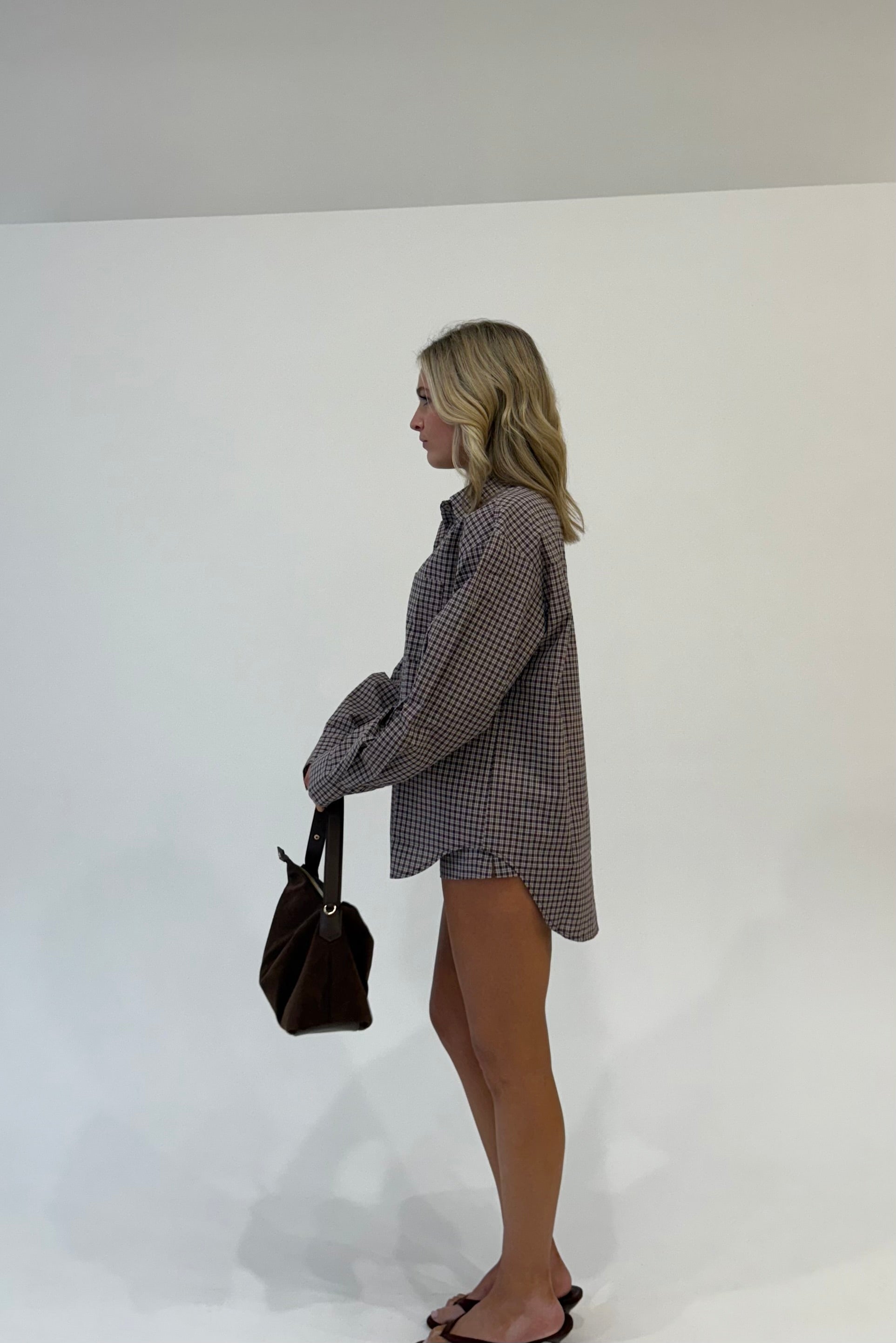 Model wearing a long-sleeve brown checkered shirt, paired with a brown handbag and sandals.