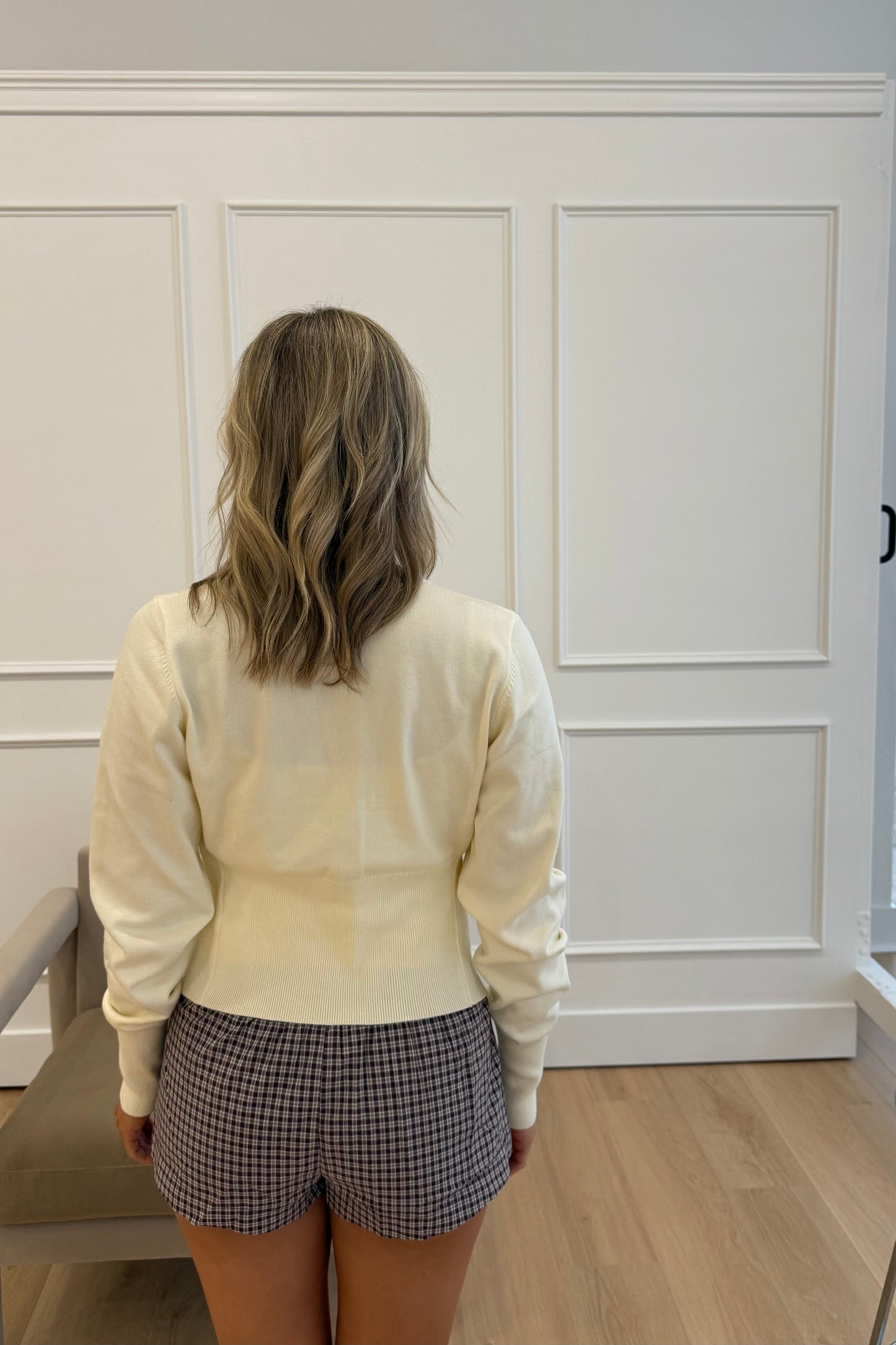 Back view of women's cream sweater, lightweight knit, paired with plaid shorts on a model.