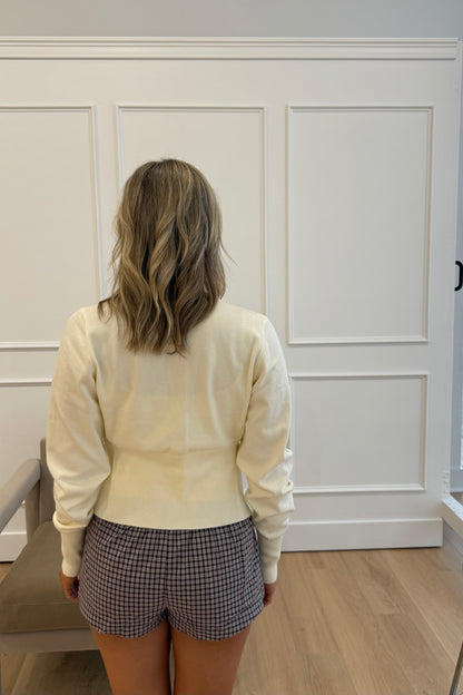 Back view of women's cream sweater, lightweight knit, paired with plaid shorts on a model.