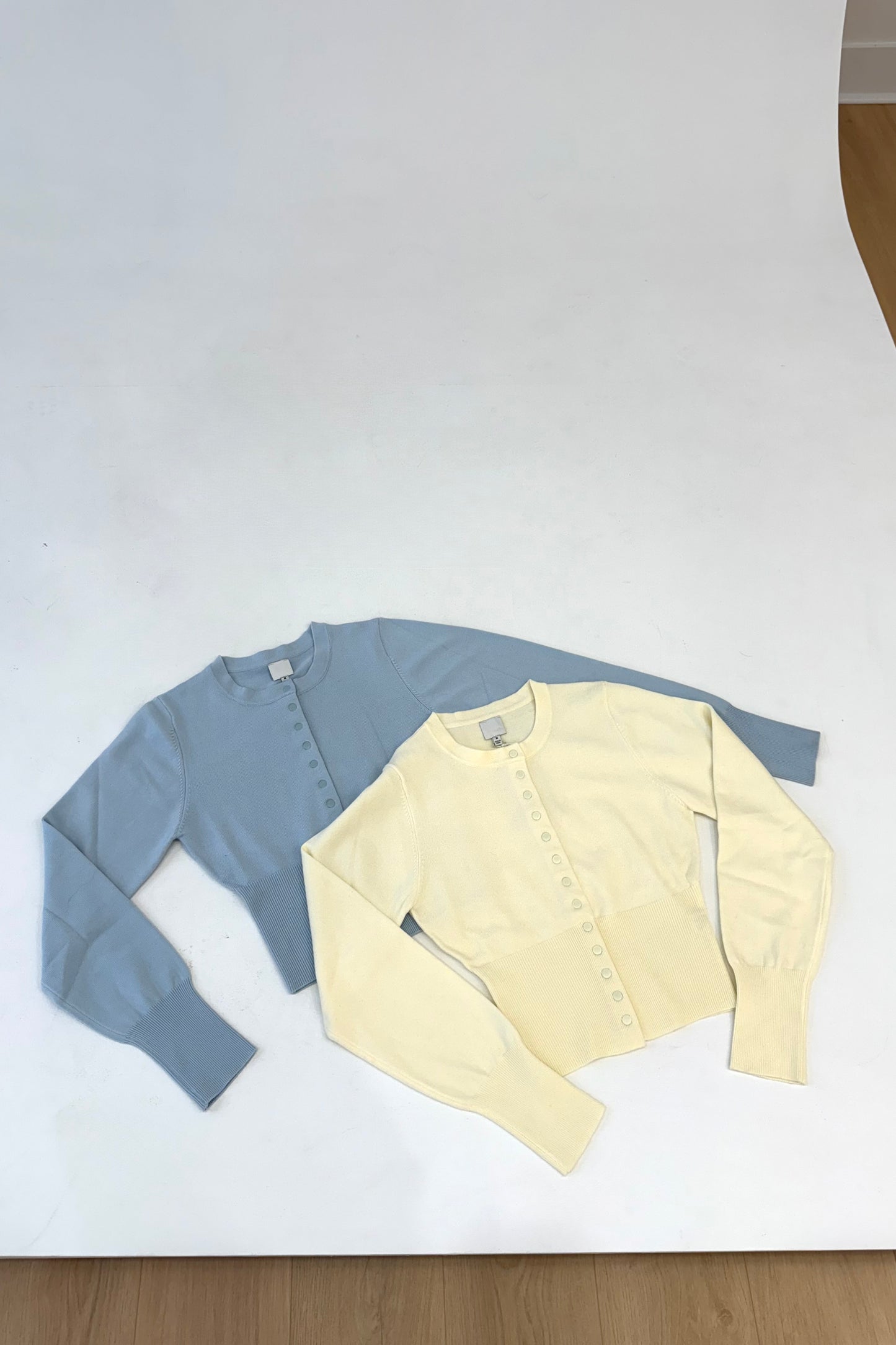 Two cropped cardigans in light blue and yellow, featuring long sleeves and button details, perfect for layering.