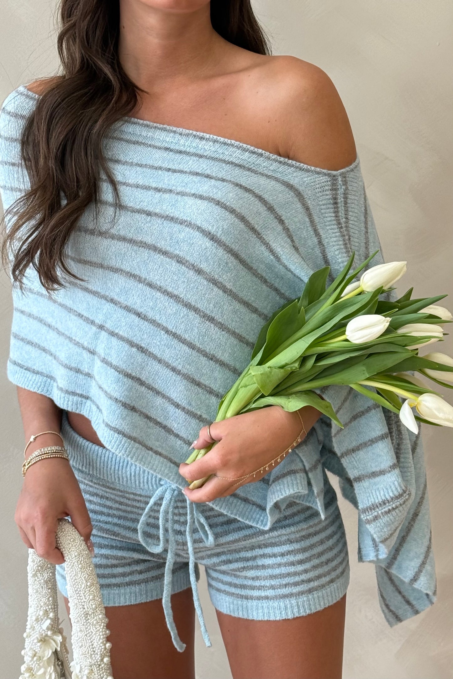 Woman wearing a light blue off-shoulder top and shorts, holding tulips.