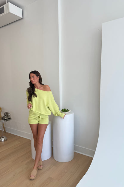 Woman in a bright yellow outfit standing in a minimalistic room with white walls and wooden floor.
