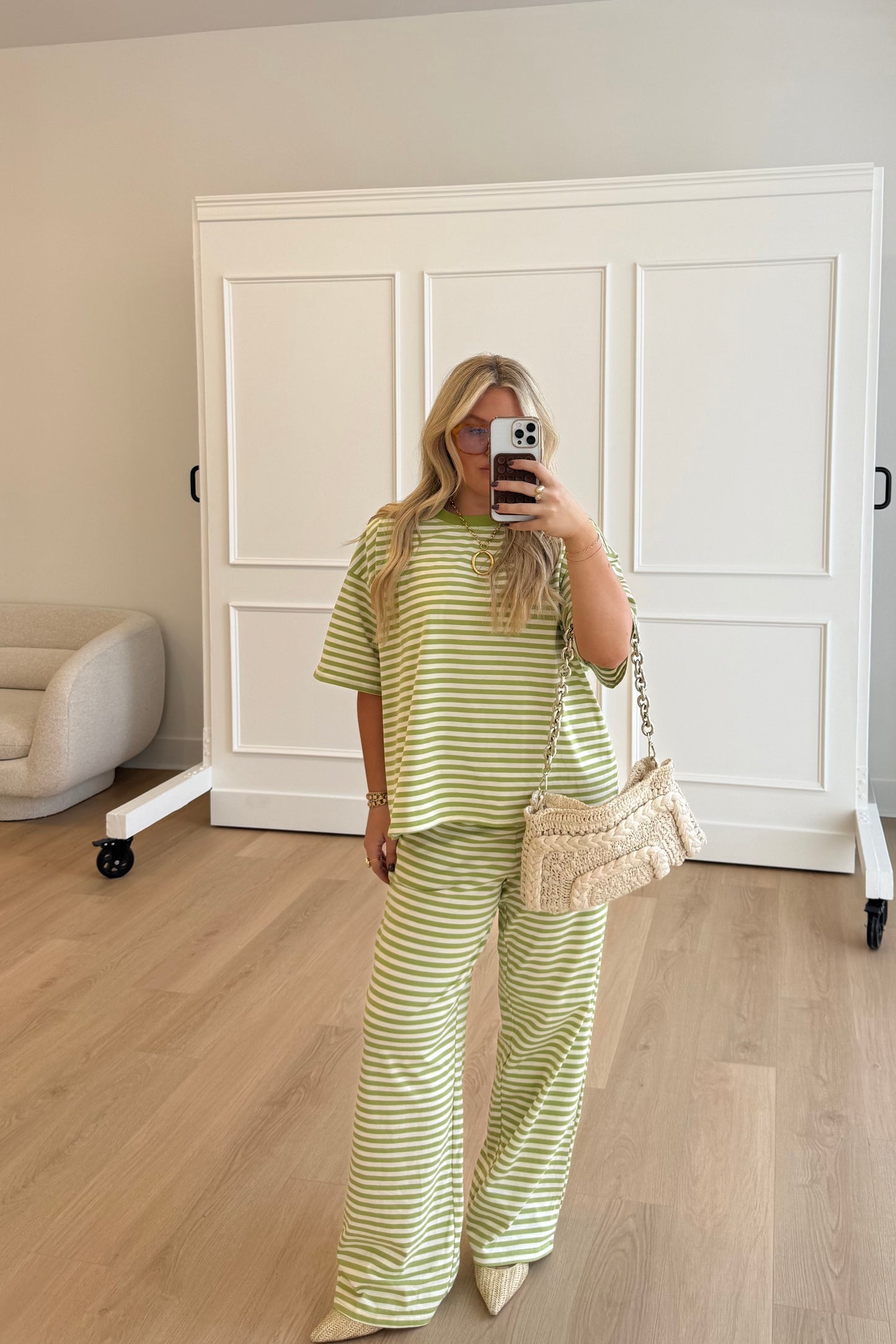 Woman taking a mirror selfie wearing a green and white striped outfit in a room with wooden flooring and white walls.