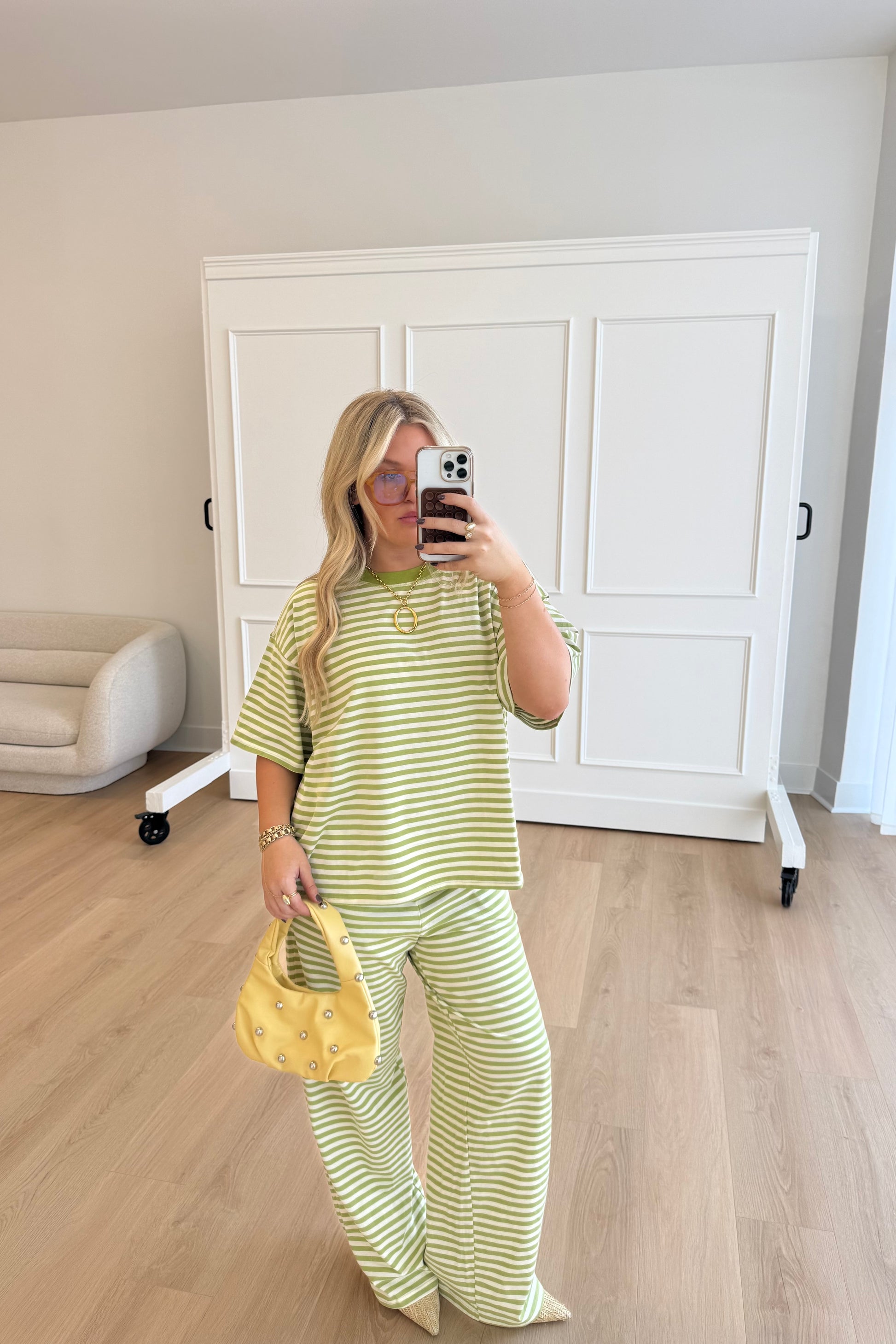 Woman taking a mirror selfie wearing a yellow and white striped outfit in a room with a white wardrobe.