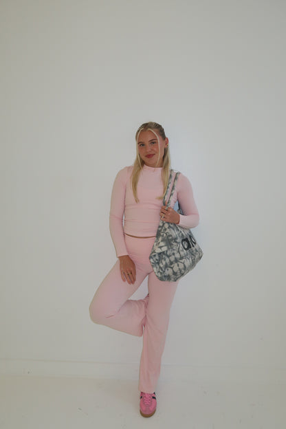 Person wearing a pink outfit with a patterned bag on a plain background