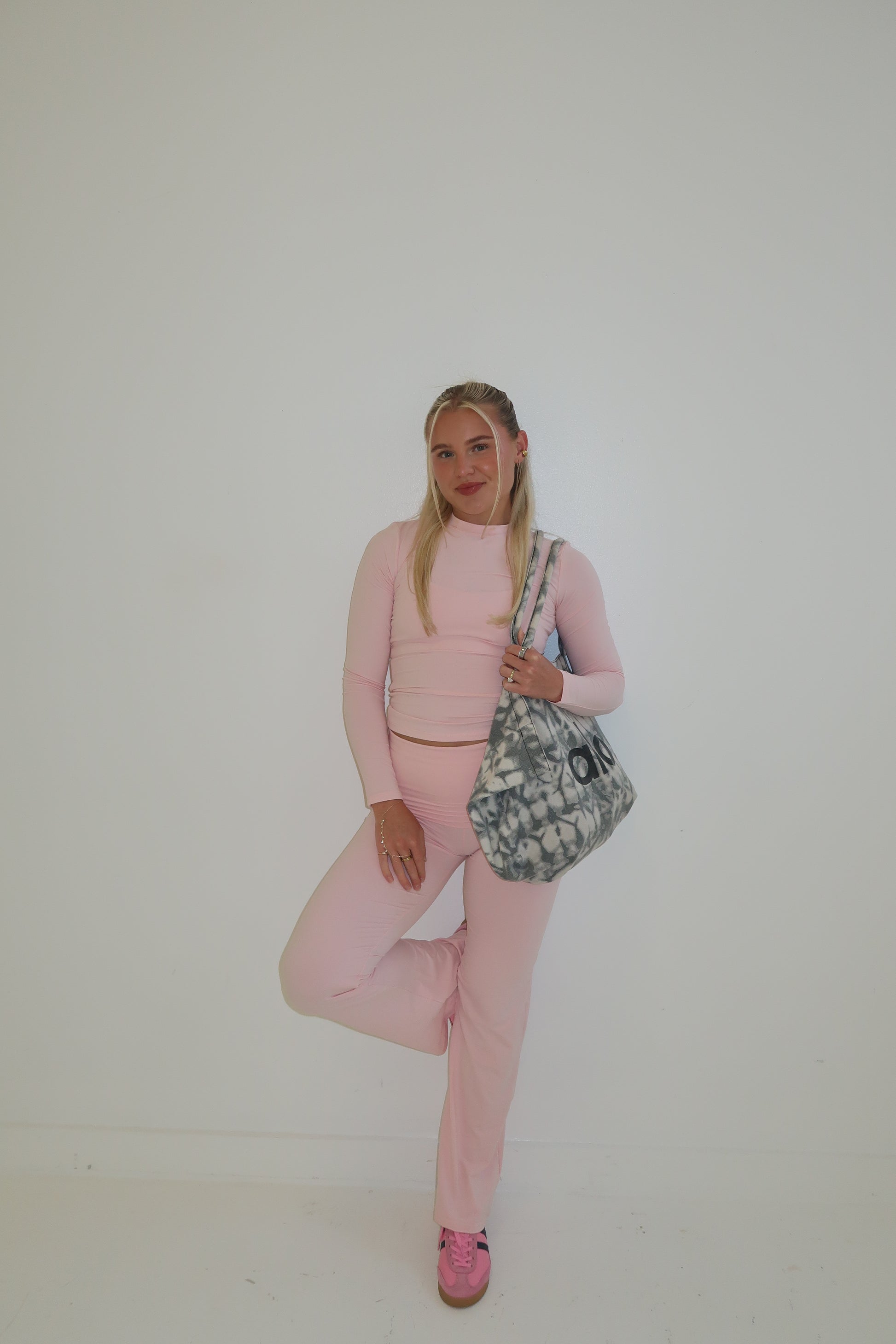 Person wearing a pink outfit with a patterned bag on a plain background