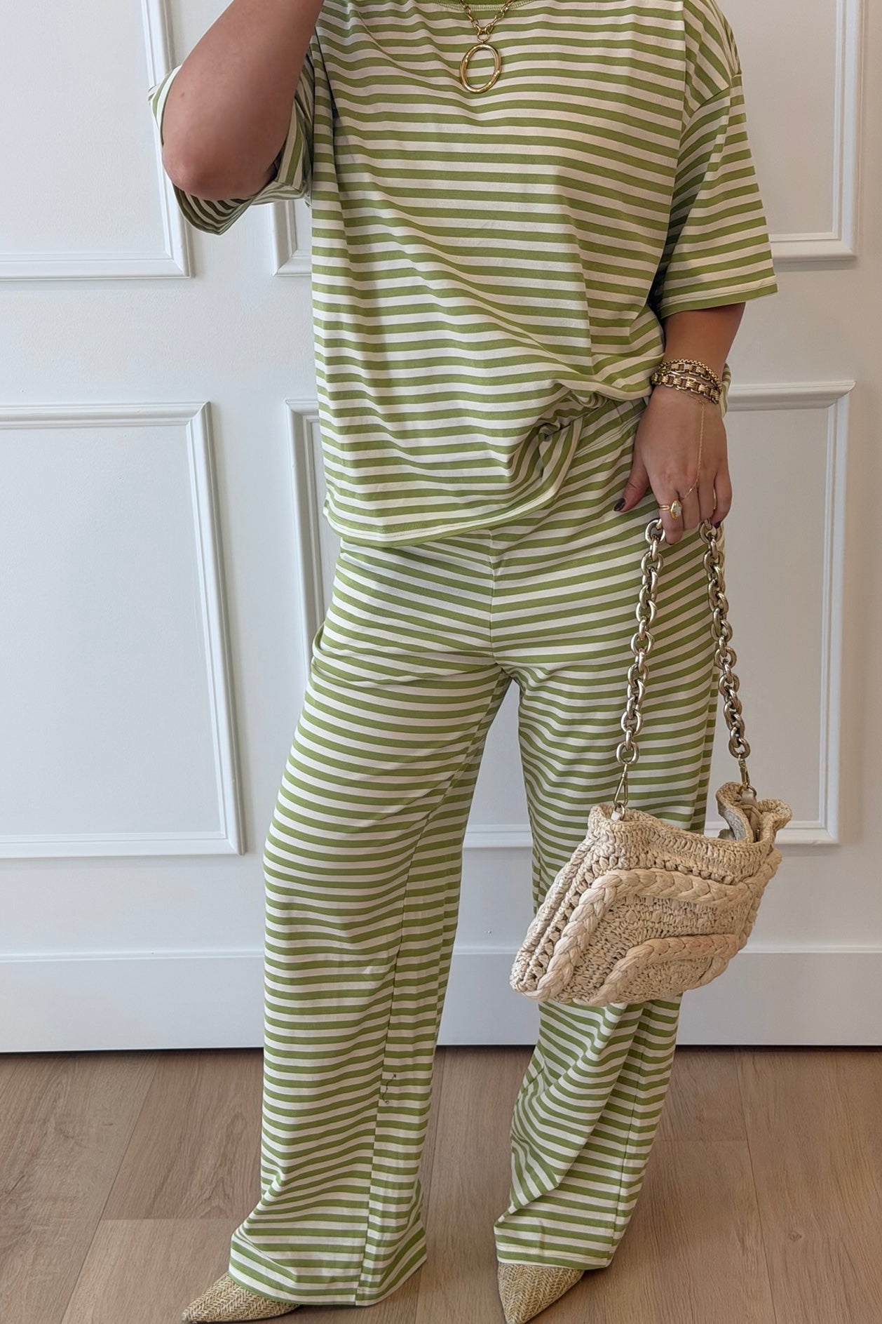 Person wearing a green and white striped outfit holding a woven handbag.
