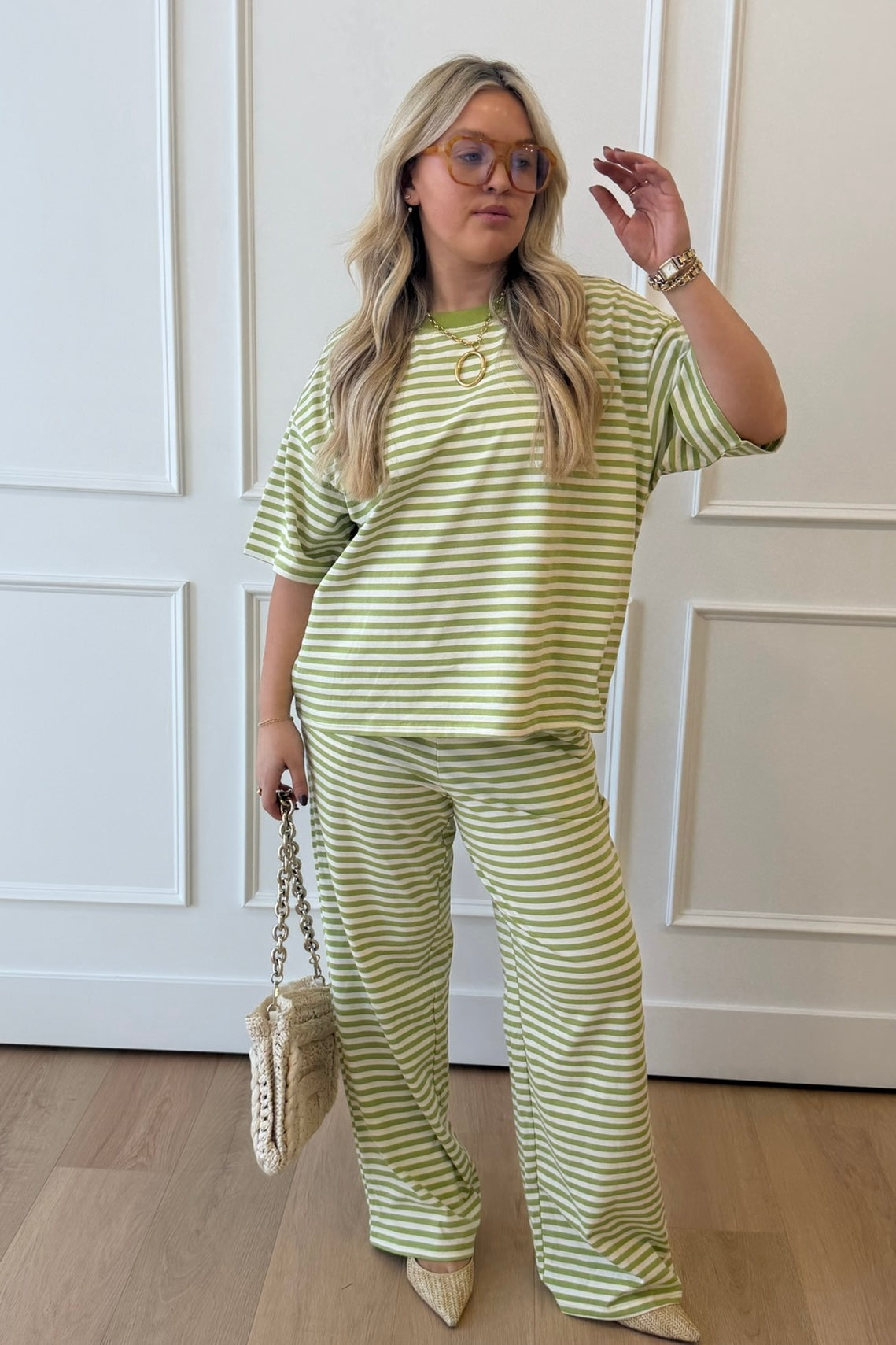 Woman wearing a green and white striped outfit standing in a room with white walls and wooden flooring.