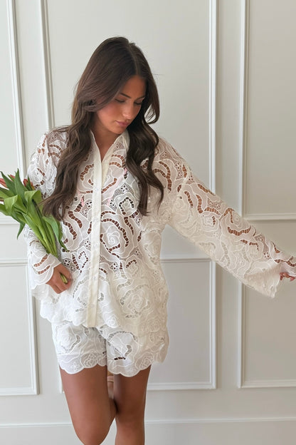 Woman wearing a white lace outfit holding tulips against a neutral background