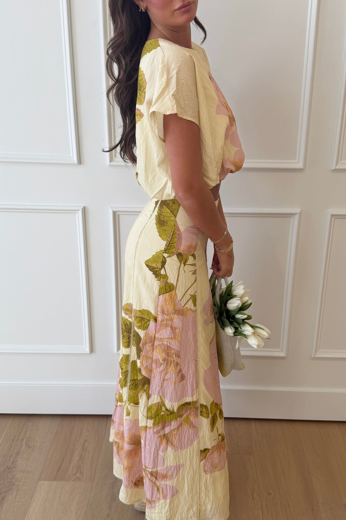 Woman wearing a floral dress holding a bouquet indoors.