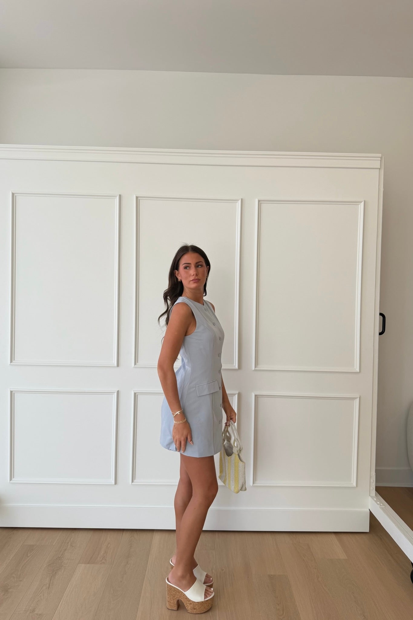 Woman in a light blue dress standing in a room with white paneled walls.