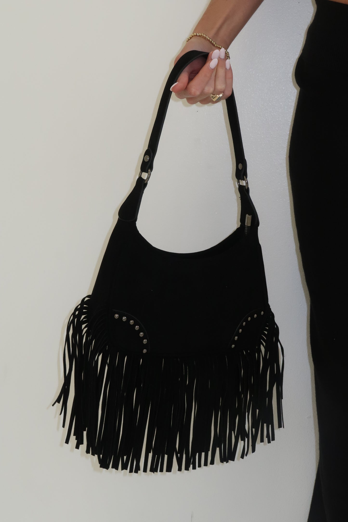 Black handbag with fringe details held by a person on a white background
