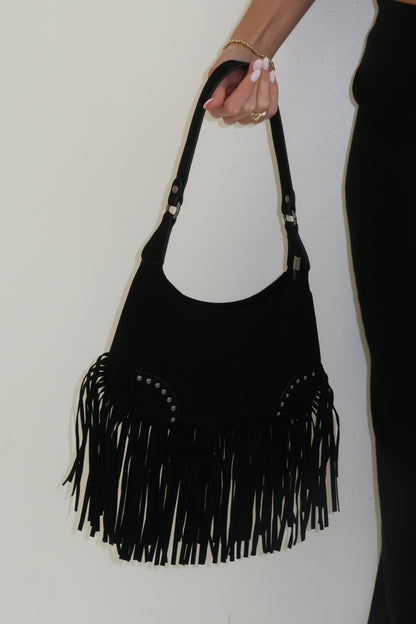 Black handbag with fringe details held by a person on a white background