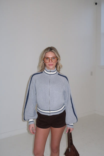 Women's gray zip-up sweater with navy stripes, featuring long balloon sleeves and styled with shorts.