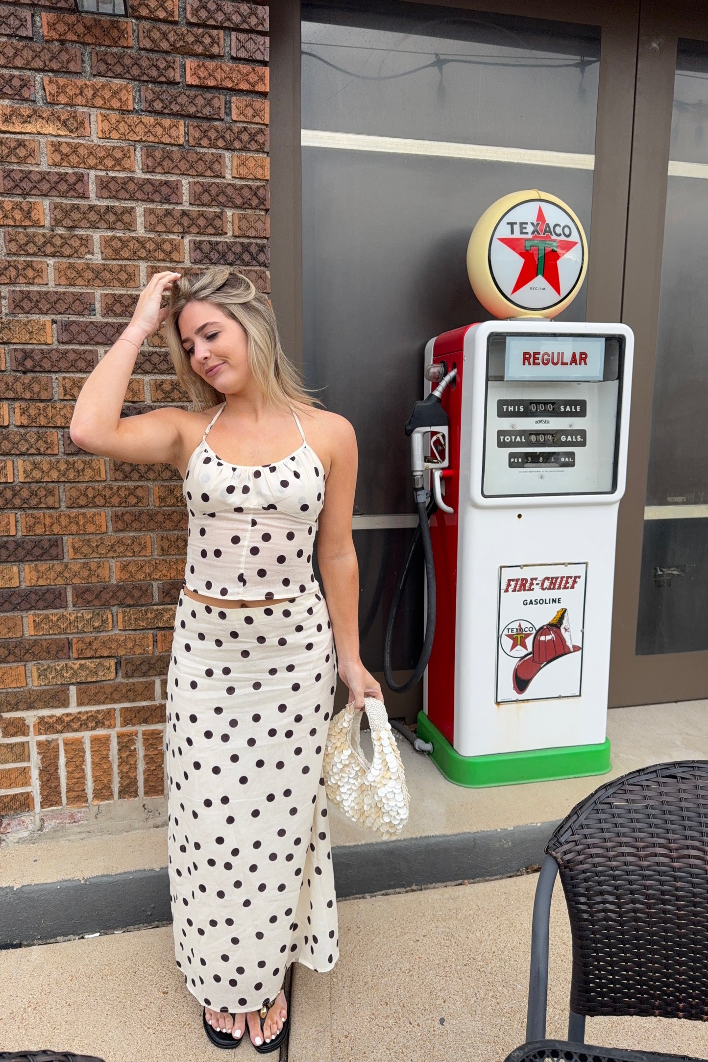 Woman in a polka dot dress standing next to a vintage gas pump with a Texaco sign.