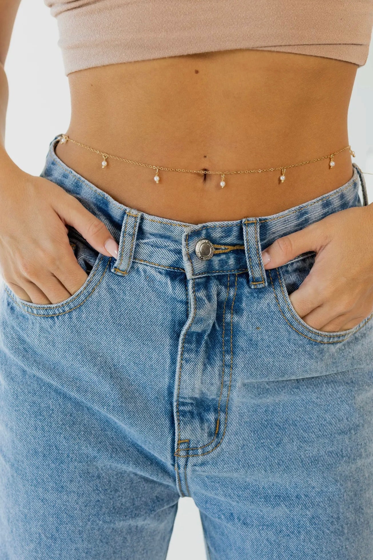 Person wearing blue jeans with a neutral background and pearl belly chain 