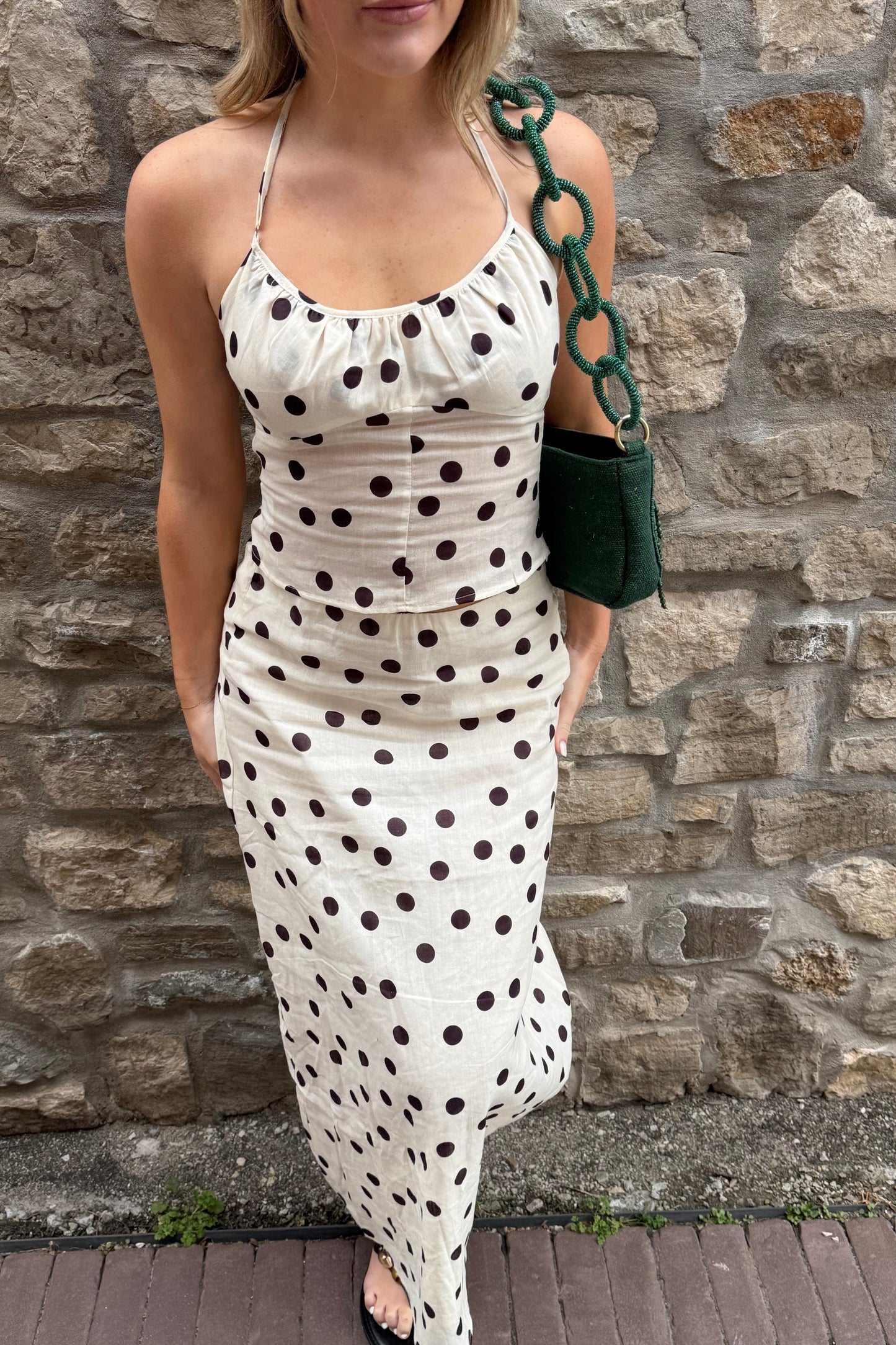 Woman wearing a polka dot dress against a stone wall.