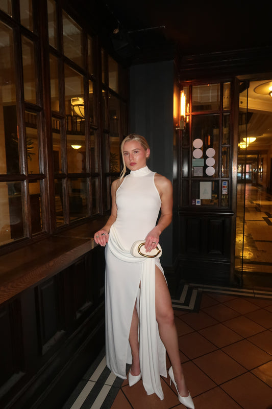 Person in a white dress standing in a dimly lit room with reflective floor.