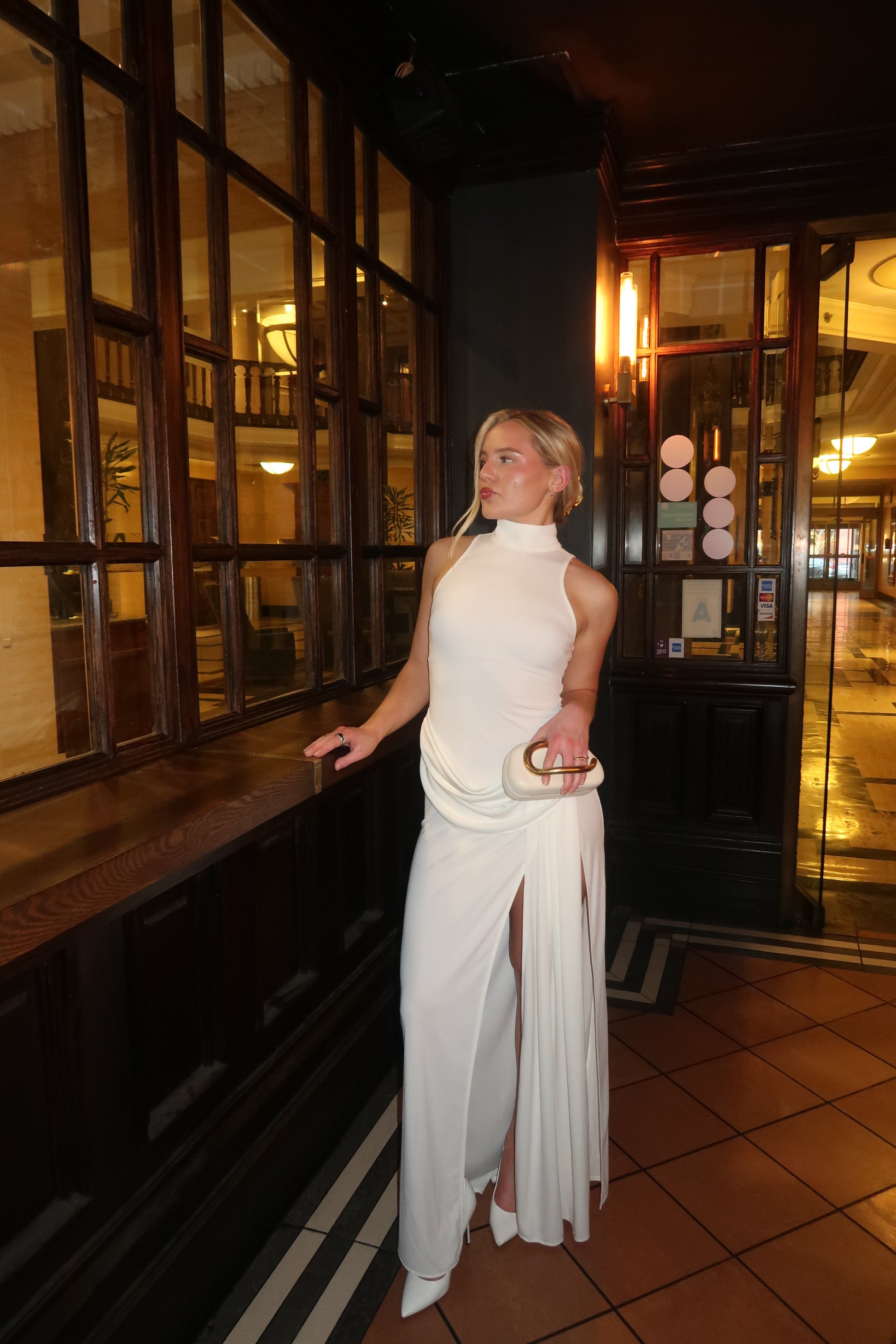 Person in a white outfit standing in a room with reflective floor and tiled walls.